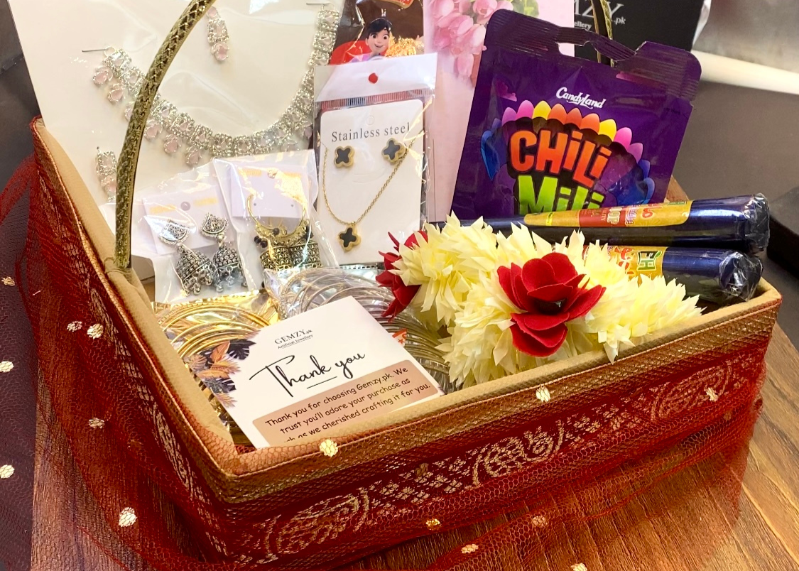 Gift basket with various items including snacks, flowers, and a card on a wooden surface.